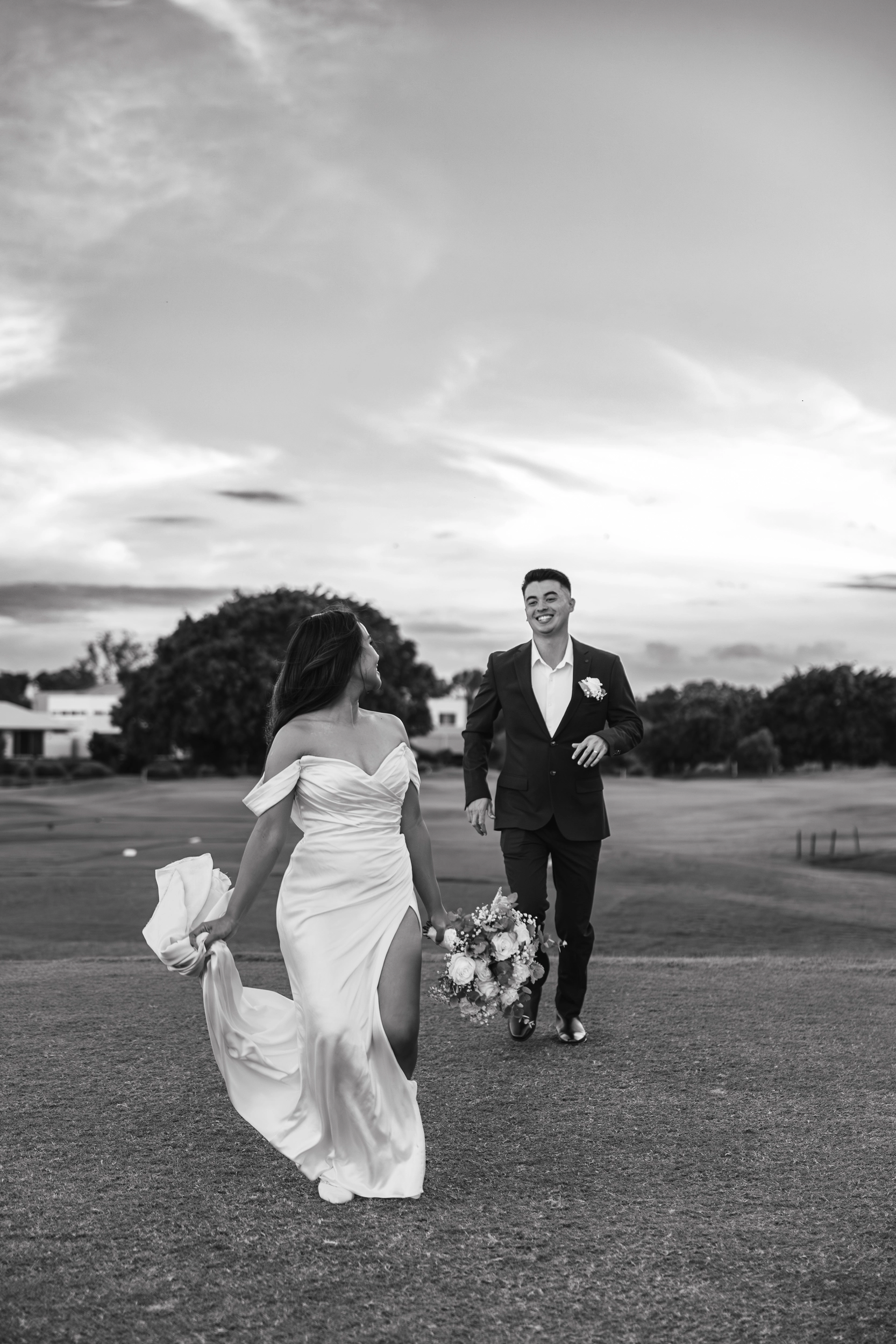 Bride and groom walking together at outdoor Brisbane wedding venue with dramatic cloudy sky