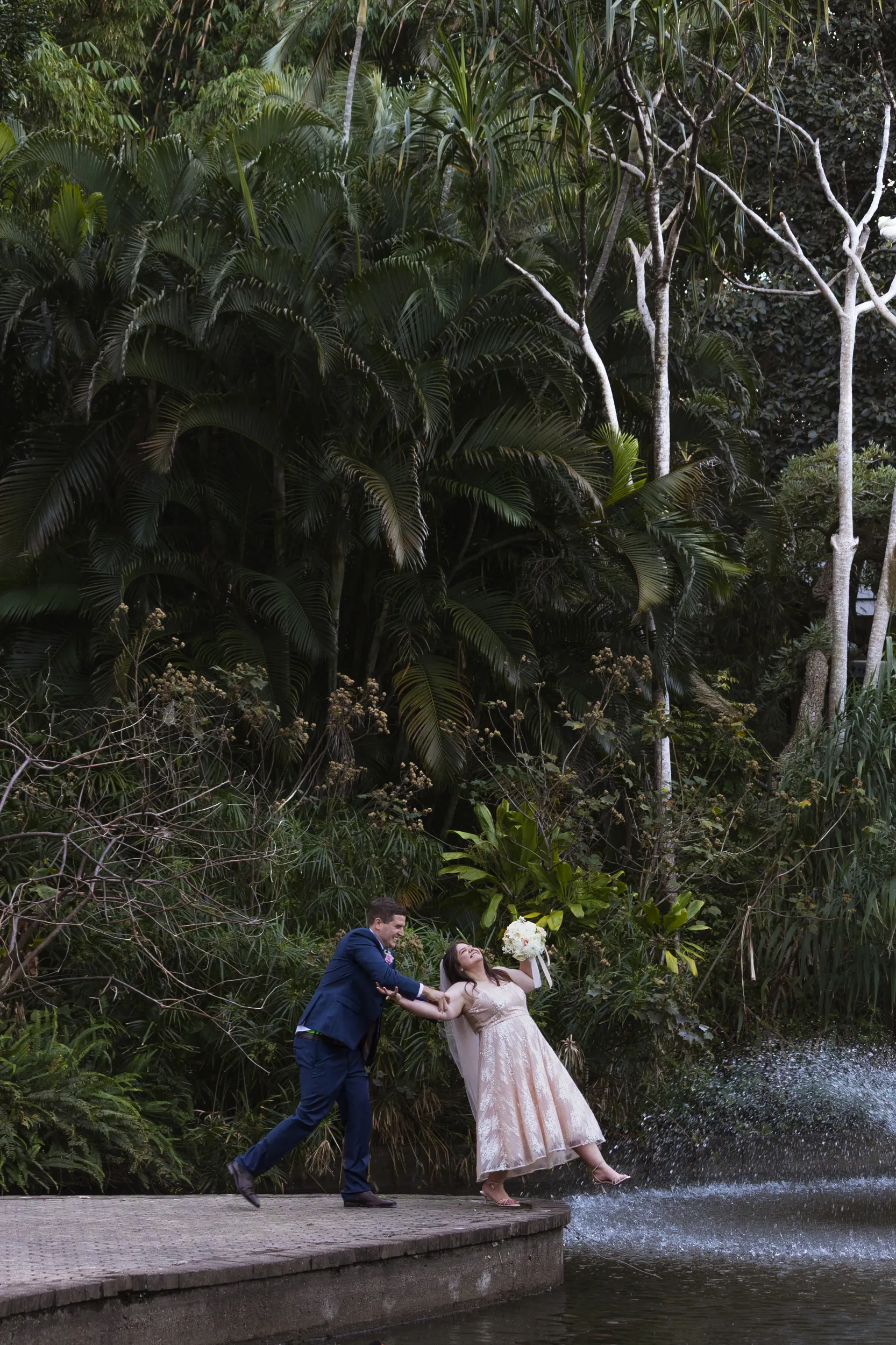 Carlie and Iain playful outdoor portrait in tropical garden with lush palm trees and dramatic pose