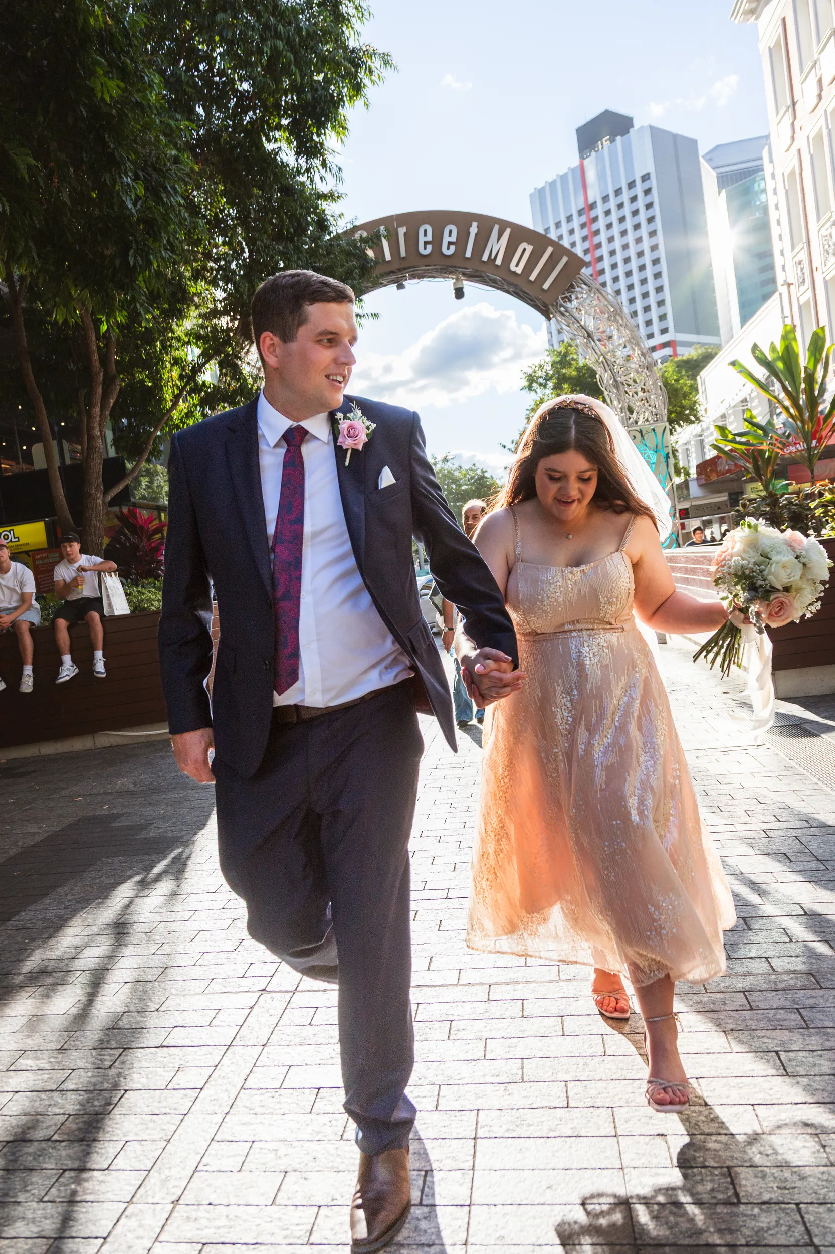 Carlie and Iain vibrant street scene walking under Street Mall archway with urban energy and city backdrop