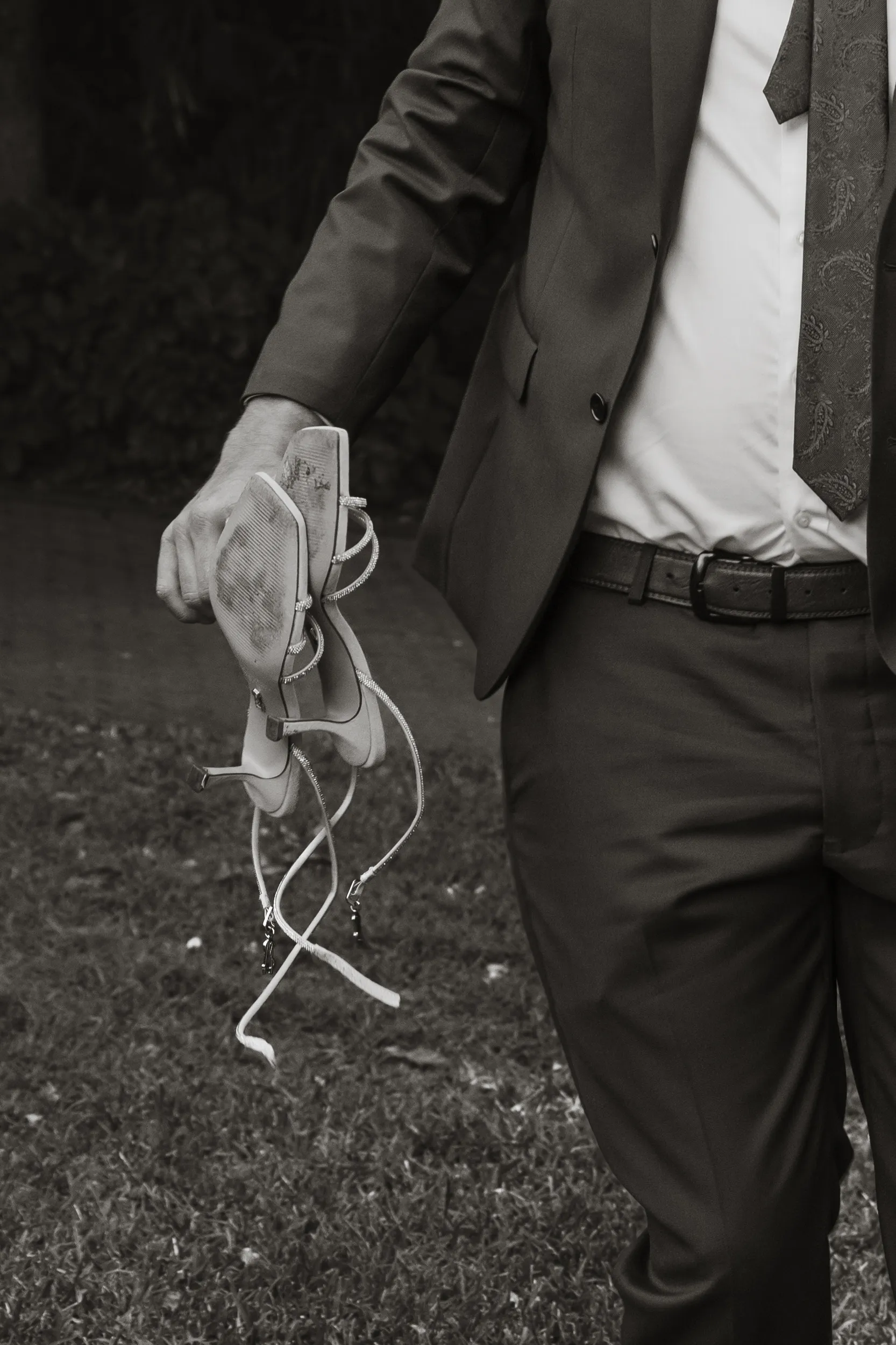Artistic black and white detail shot of Iain holding Carlie's elegant strappy high-heeled wedding shoes