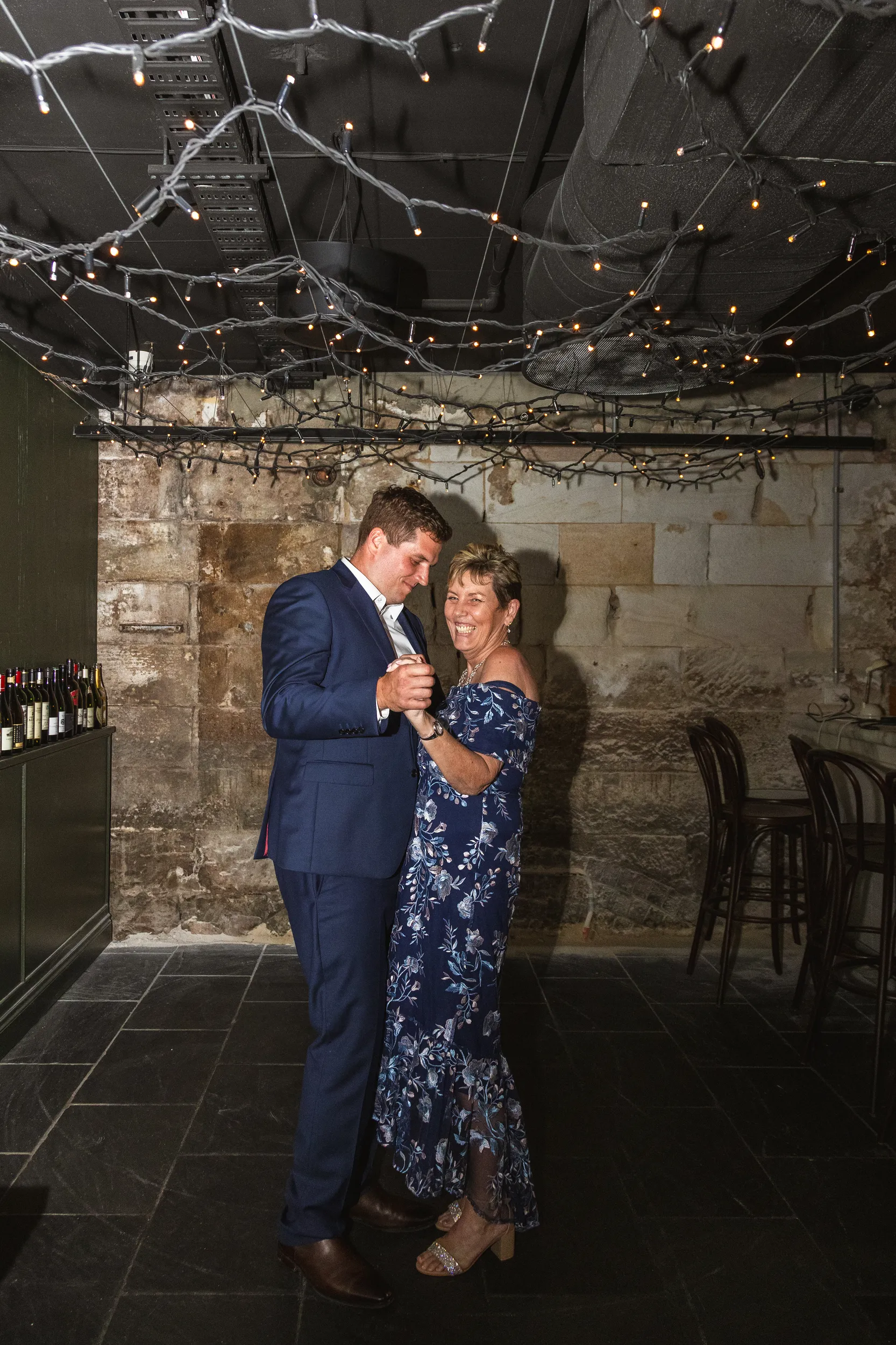 Iain heartwarming dance with mother in rustic cellar venue with string lights and exposed brick walls
