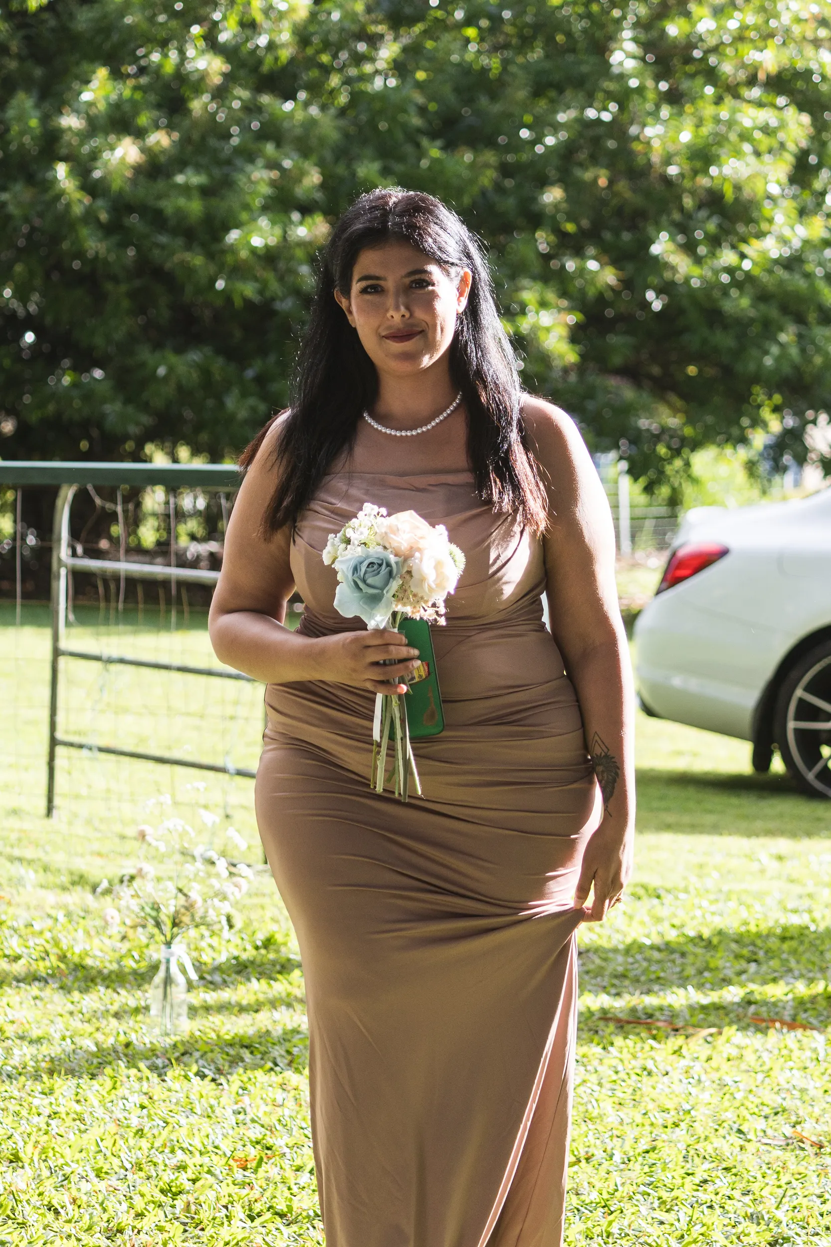 Bridesmaid in taupe dress wearing pearl necklace and holding bouquet with blue and white flowers