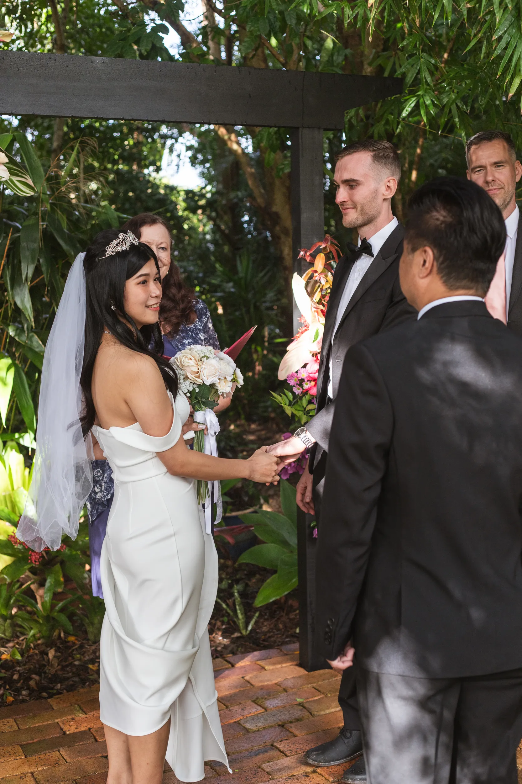 Huiyu and Chris ceremony moment exchanging vows under wooden pergola with family and officiant present