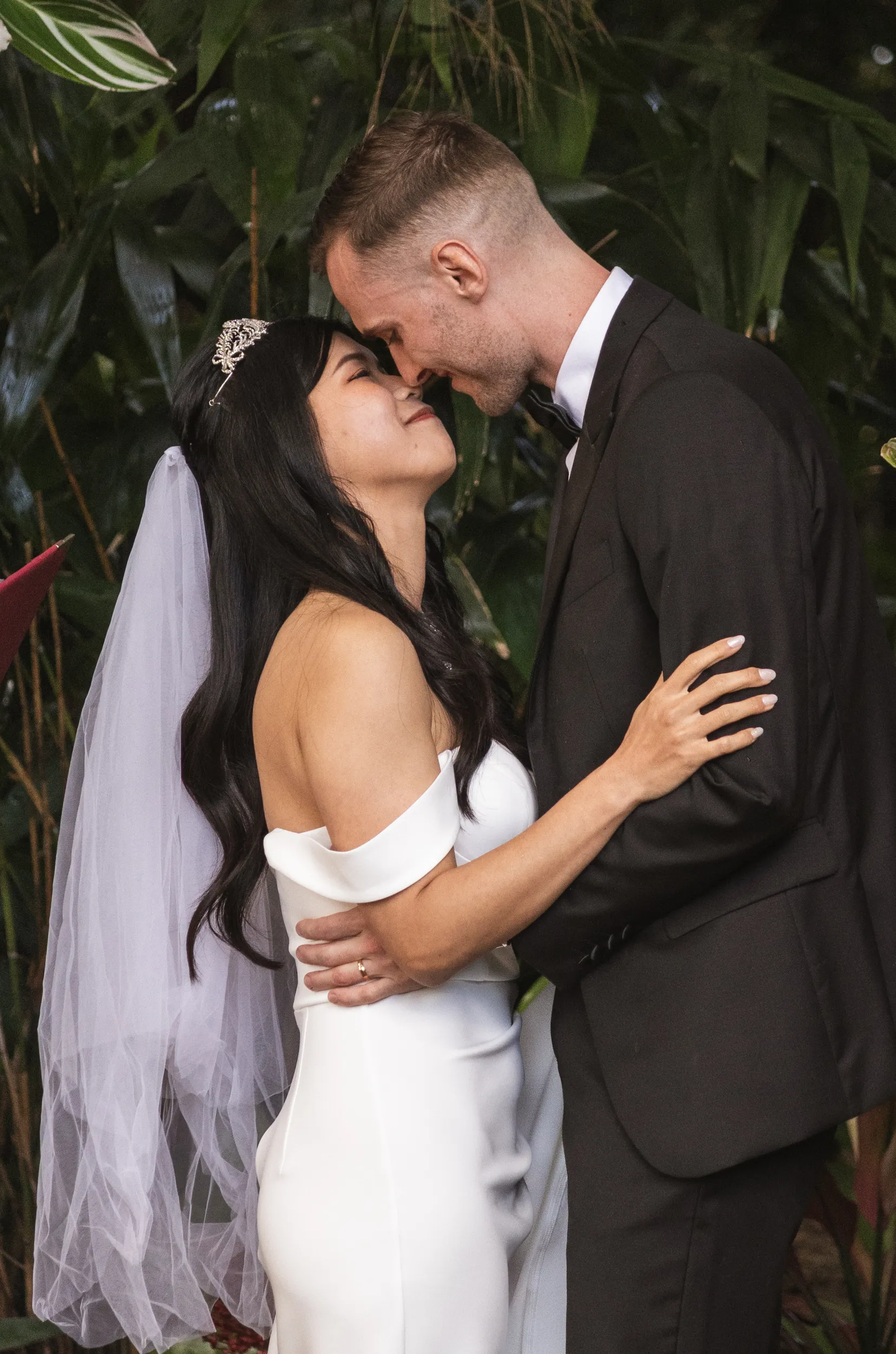 Huiyu and Chris intimate moment about to kiss in garden with bride's crystal tiara and lush green foliage backdrop