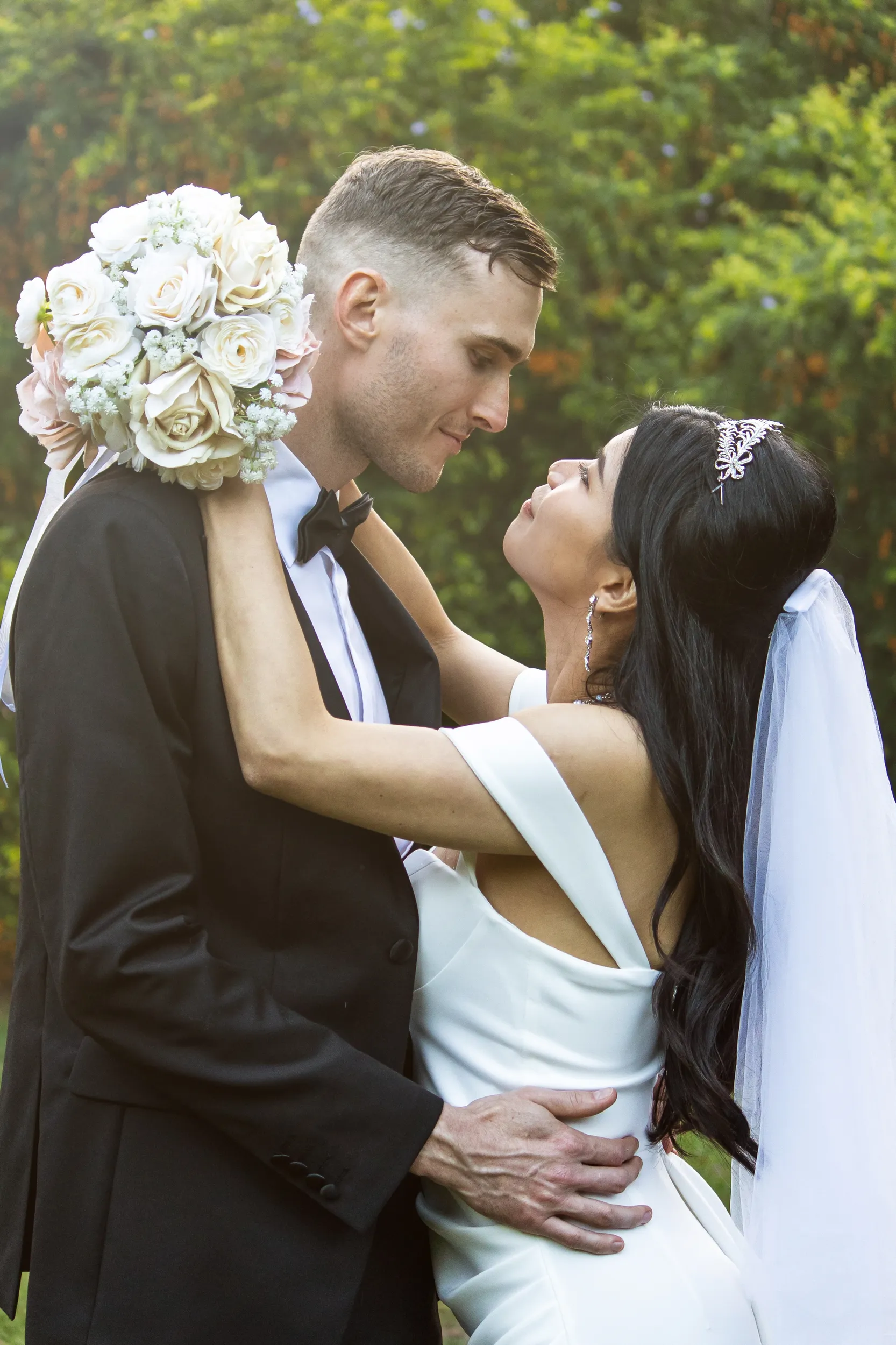 Huiyu and Chris romantic portrait embracing with bride holding white rose bouquet and wearing crystal tiara