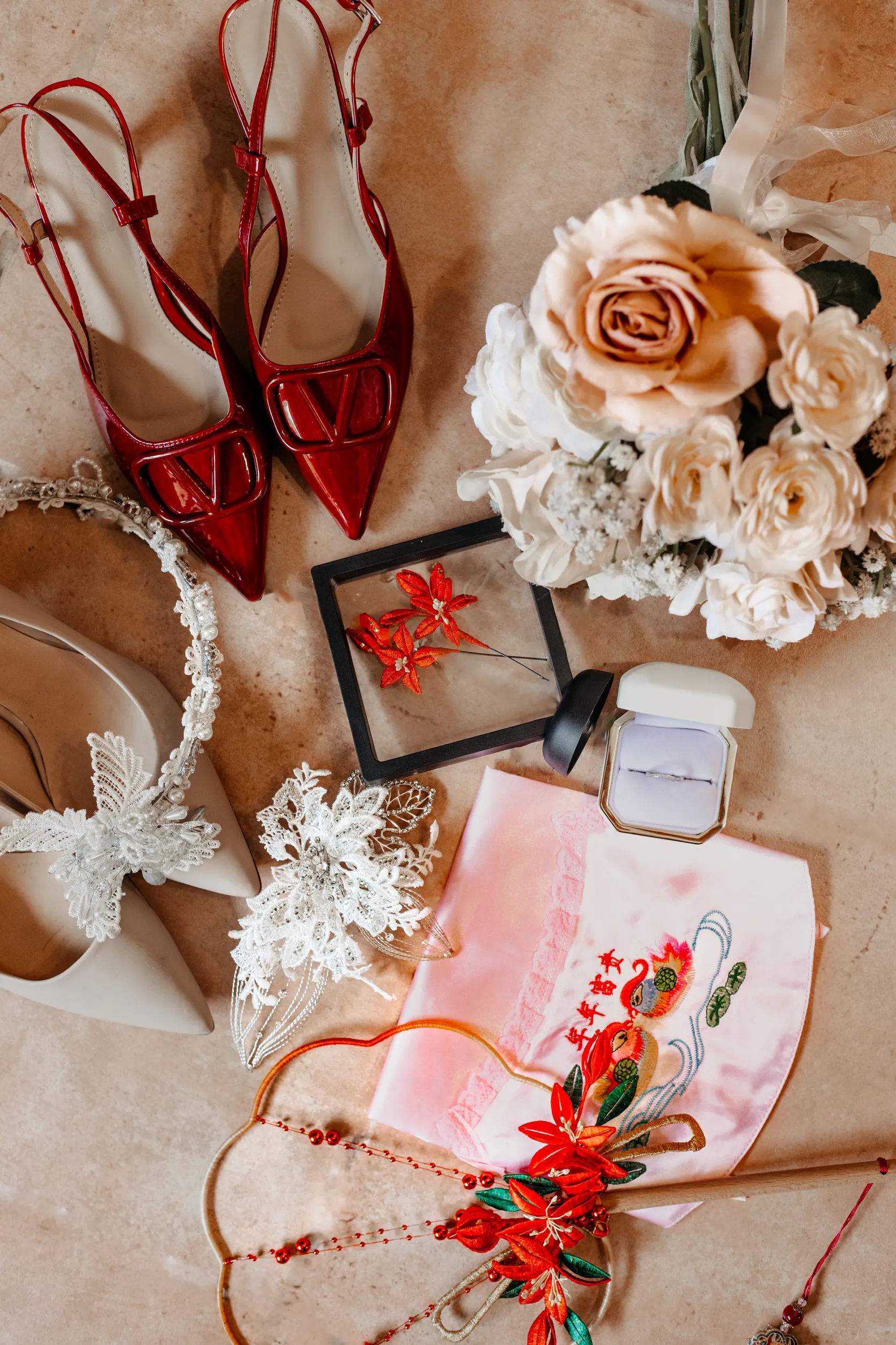 Huiyu and Chris wedding details flat lay with red Valentino heels, white roses bouquet, wedding rings, and traditional Chinese elements