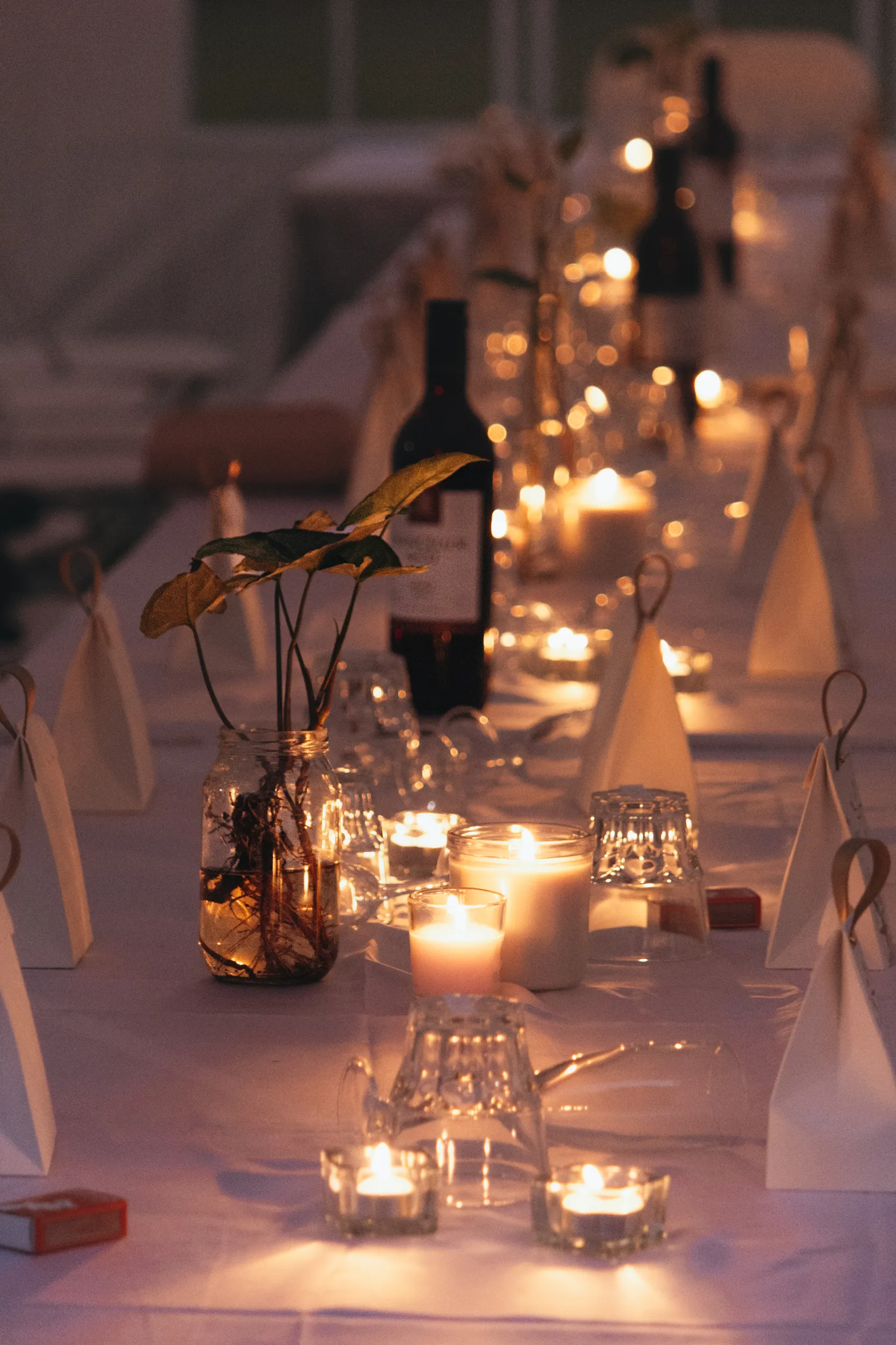 Romantic wedding reception table setting with warm candlelight, glass vases with greenery, wine bottles and elegant decorations