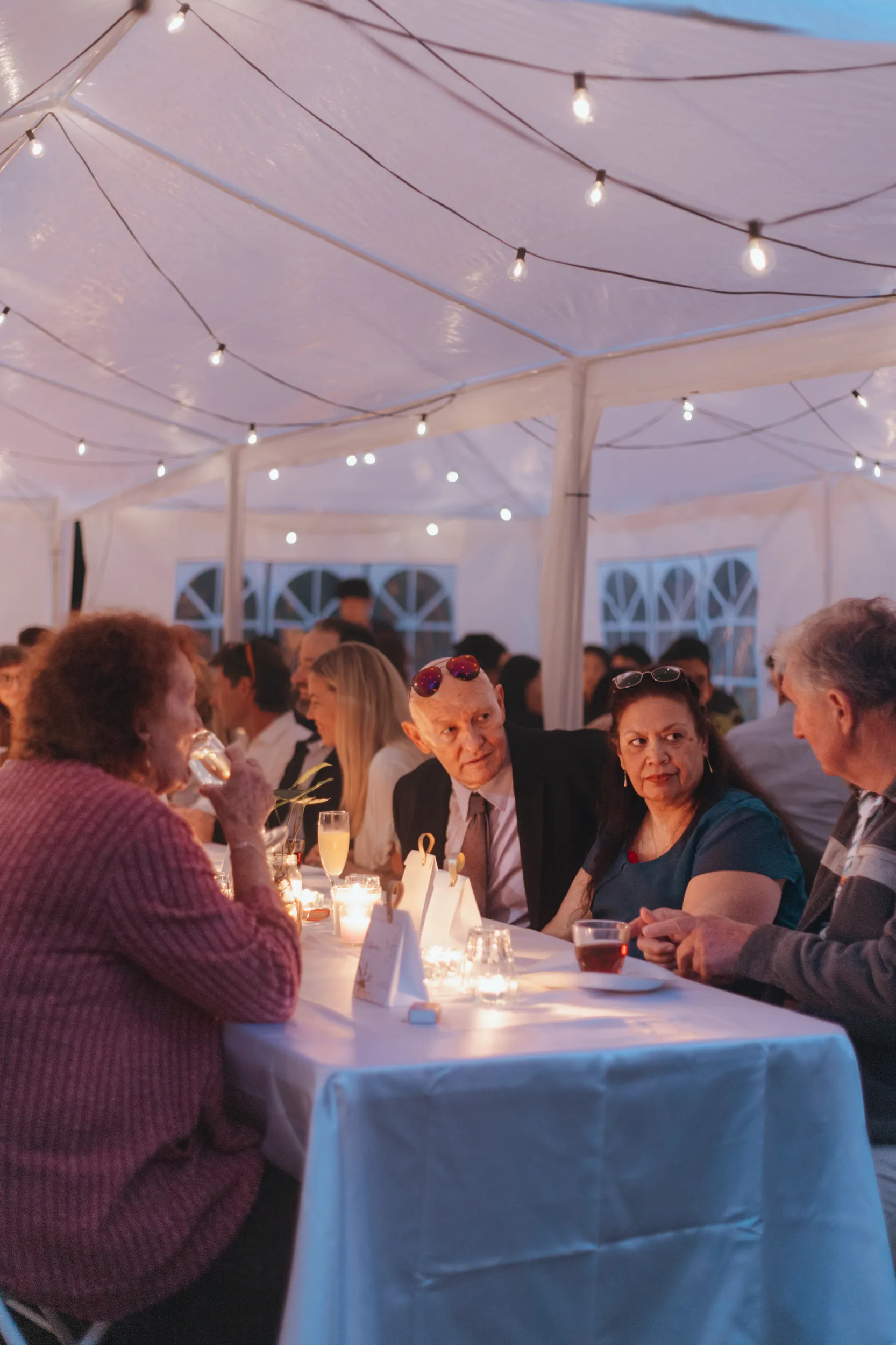 Huiyu and Chris wedding reception under white tent with string lights and guests enjoying dinner
