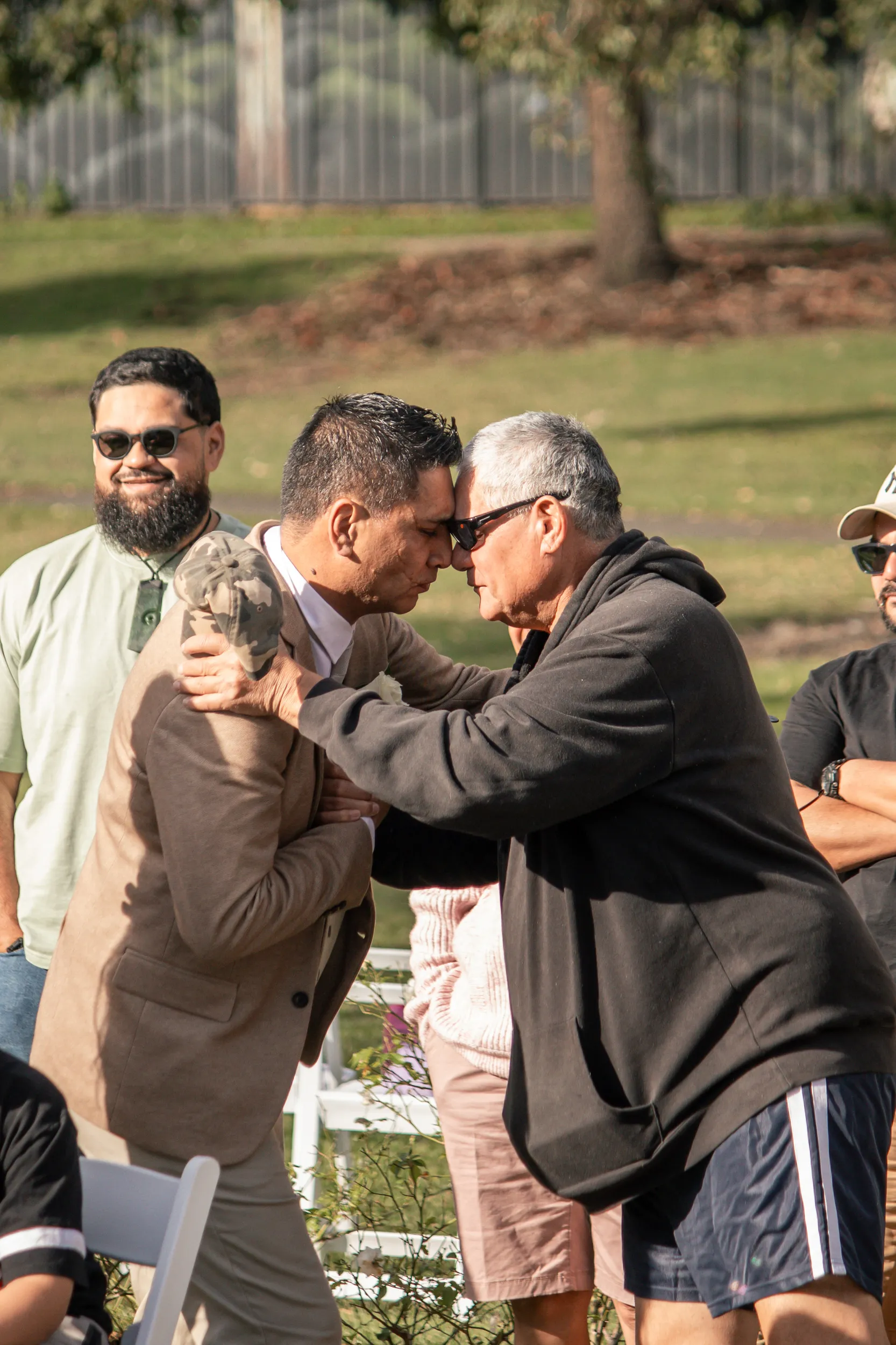 Traditional Māori hongi greeting between groom and elder during wedding ceremony with family watching