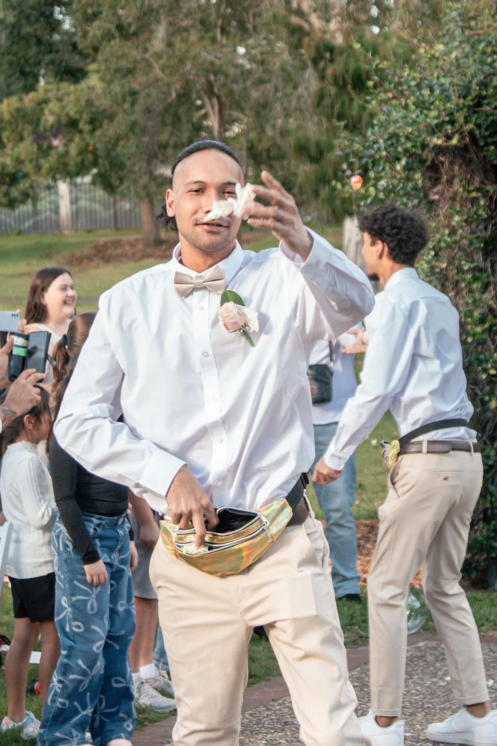 Joyful groomsman waving to guests while holding traditional carved bowl during wedding celebration