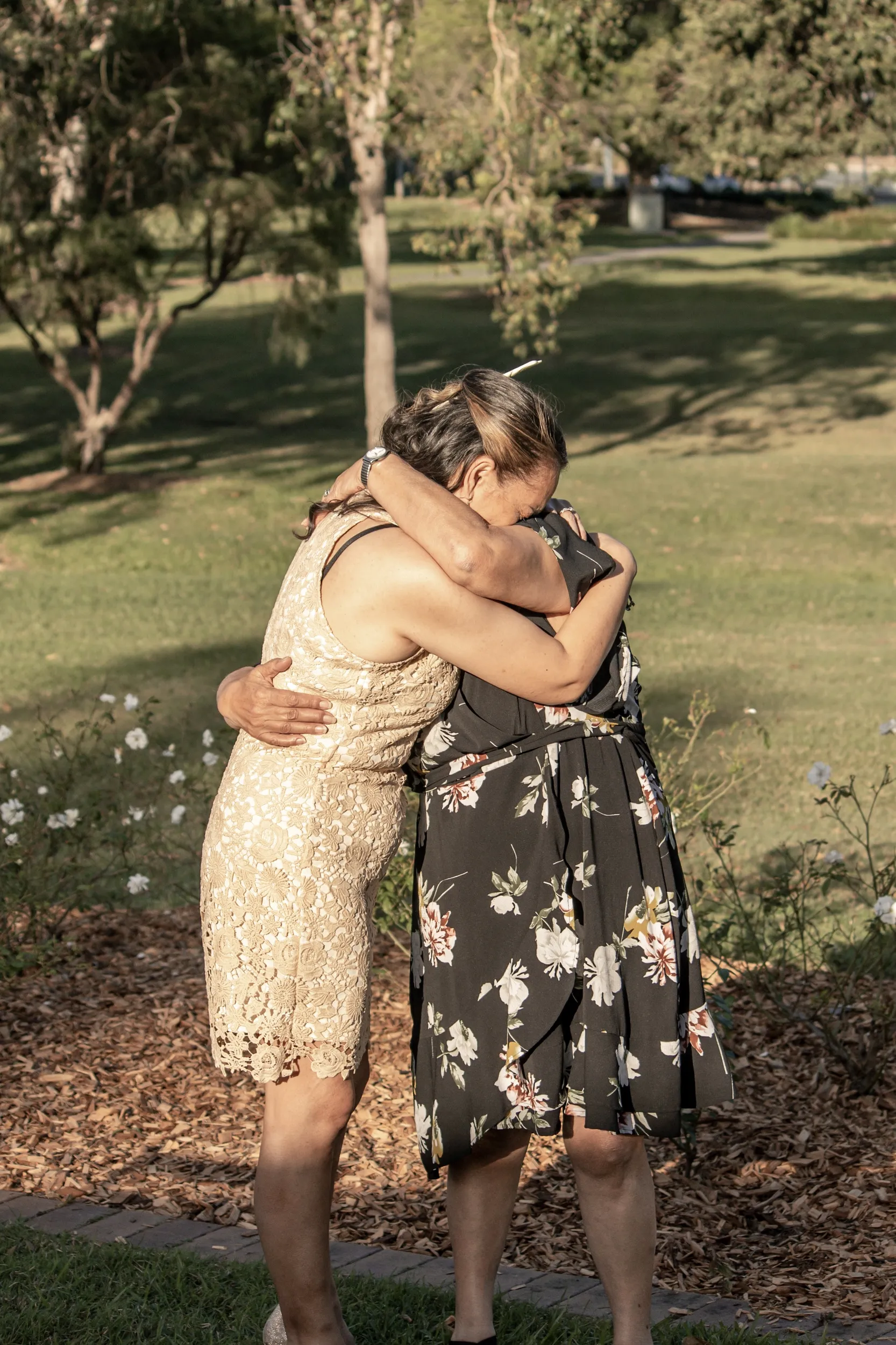 Emotional wedding moment with bride embracing family member in floral dress in beautiful park setting