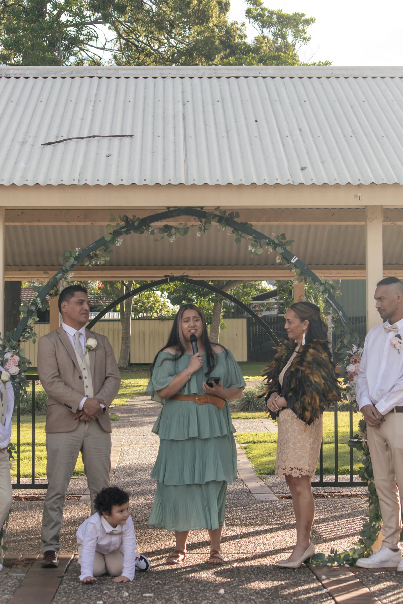 Family-centered wedding ceremony under pavilion with child sitting and bride in traditional cloak