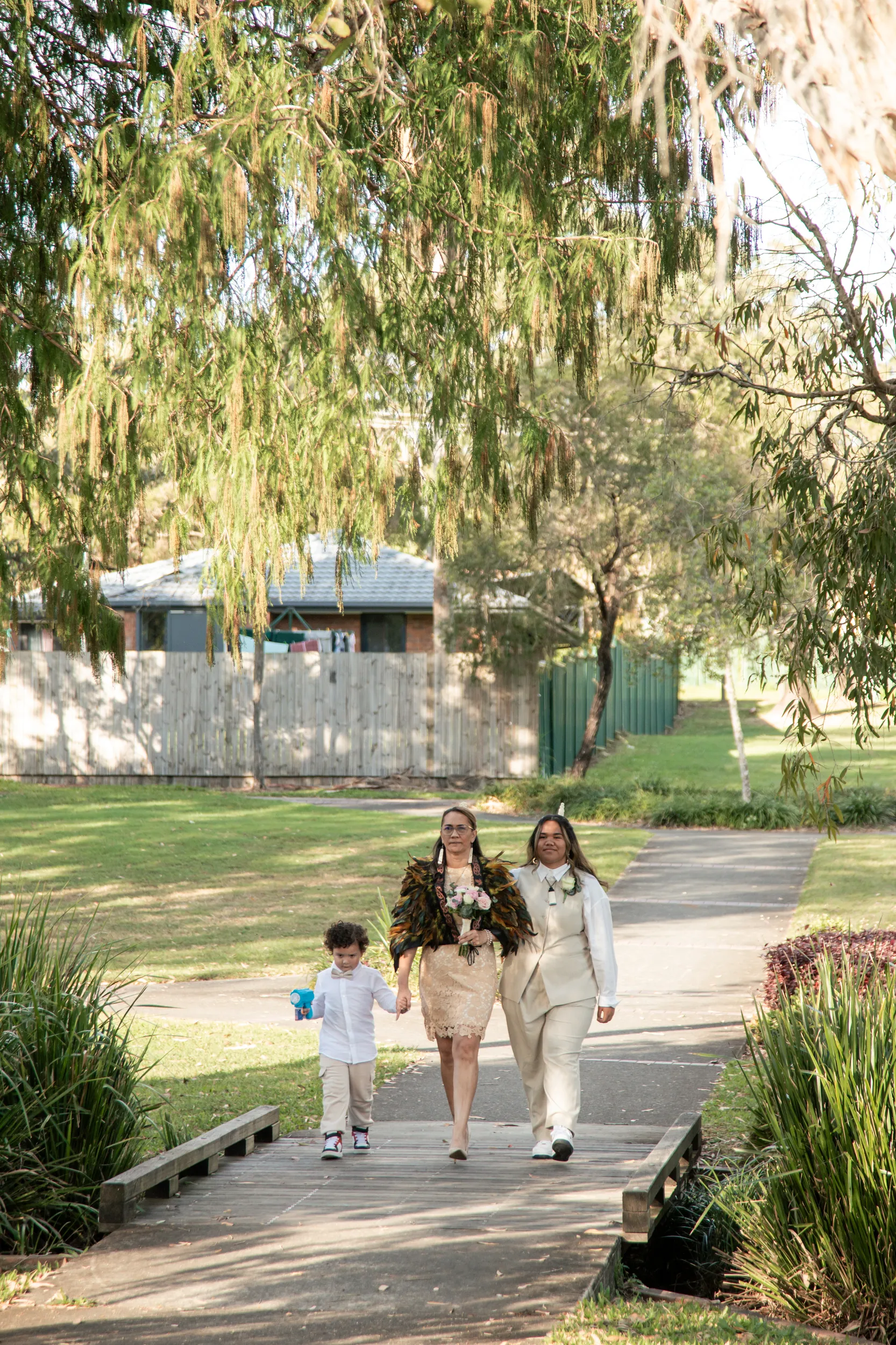 Heartwarming family moment with bride in traditional feather cloak walking with woman and child on boardwalk