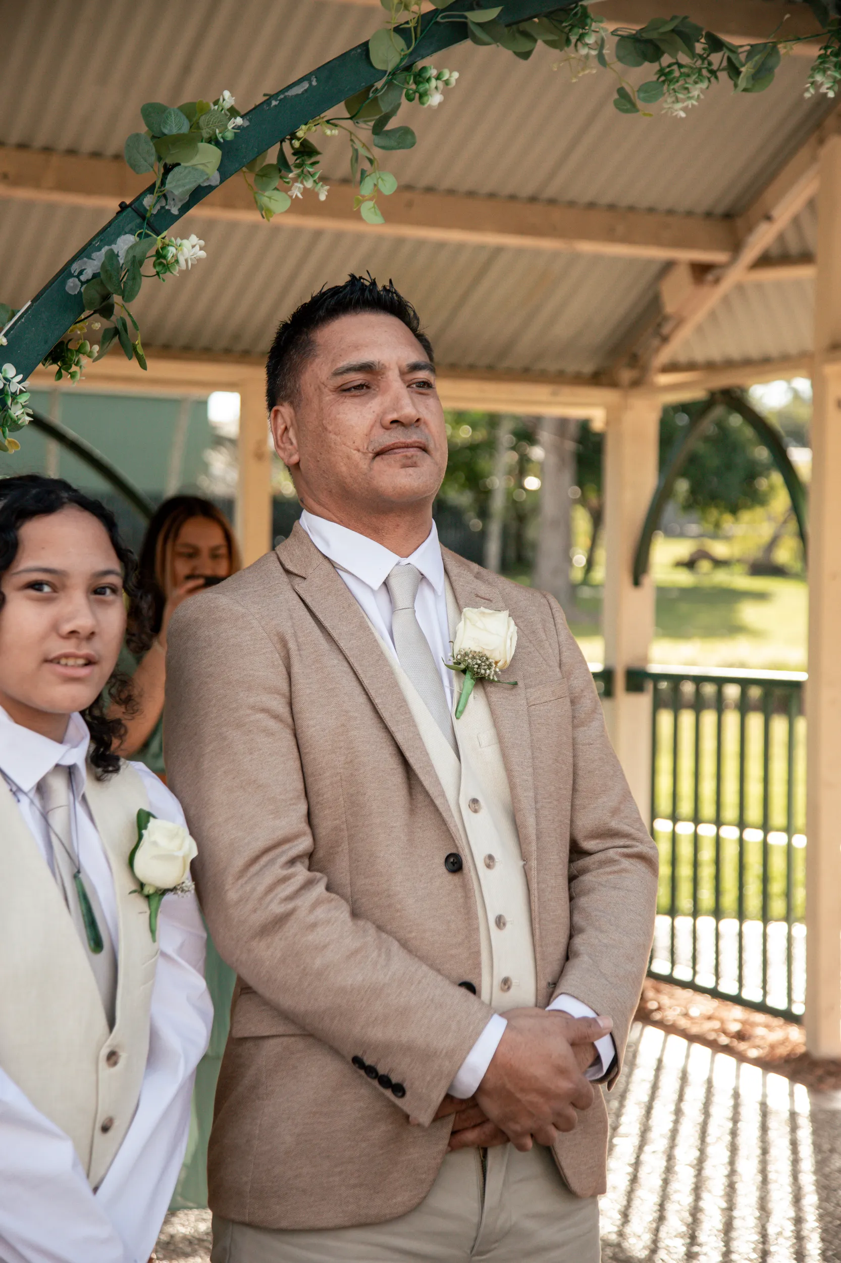 Emotional wedding ceremony moment with groom looking touched during vows under floral arch