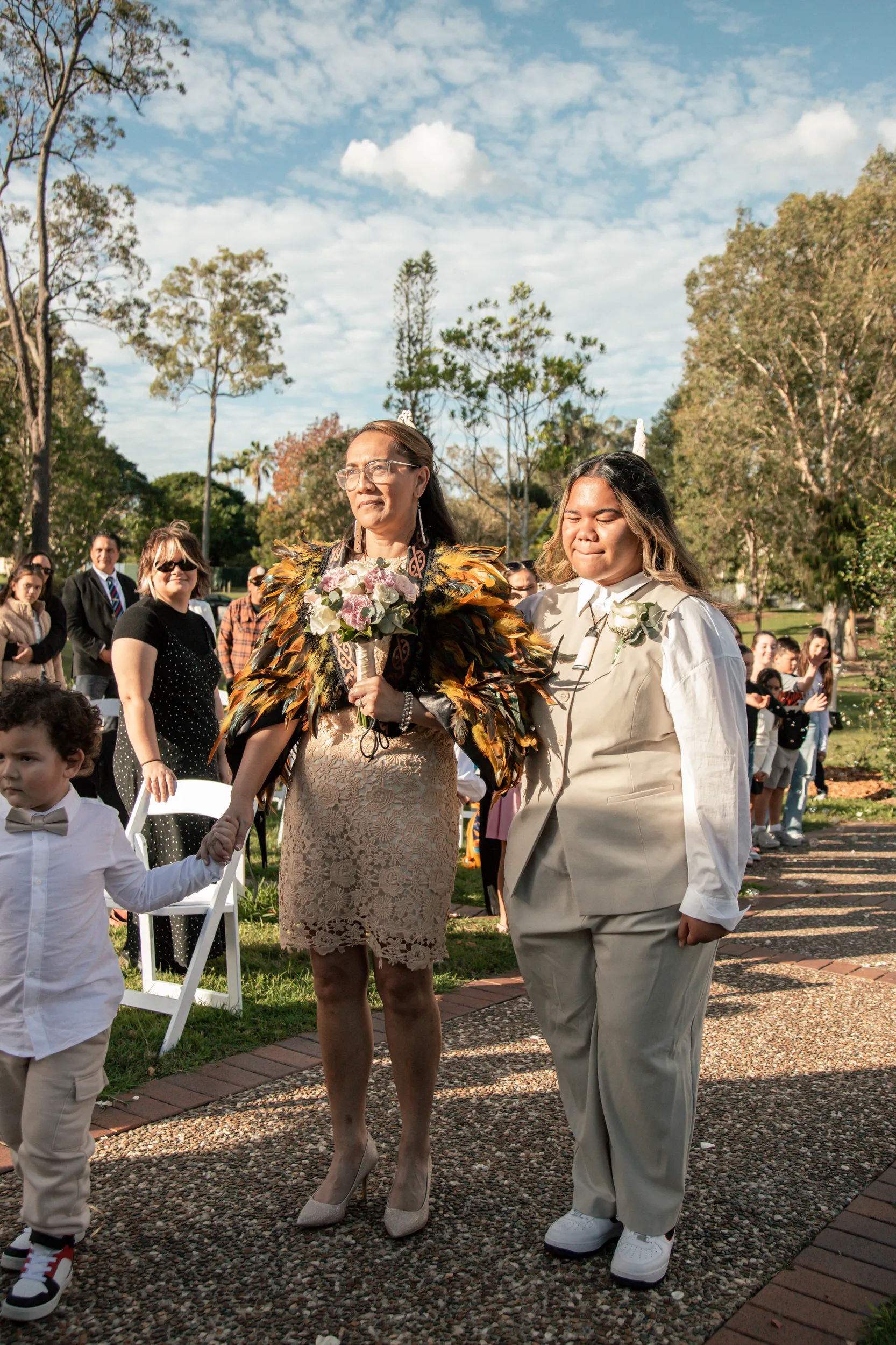 Wedding processional with bride in traditional Māori feather cloak walking down aisle with seated guests